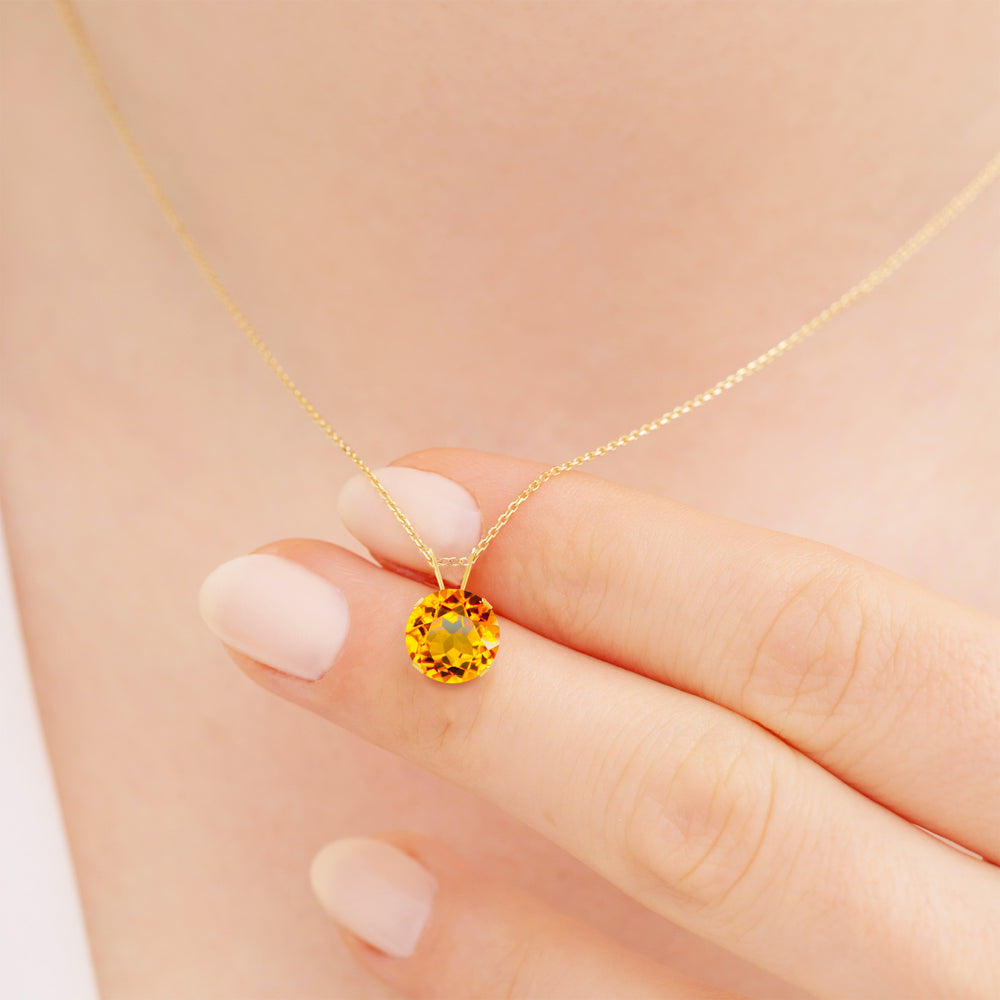 Hand holding an 8mm round citrine pendant necklace in 14K solid yellow gold, with 4-prong setting and cable chain.
