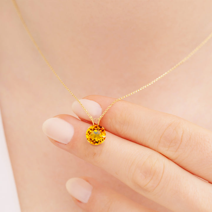 Hand holding an 8mm round citrine pendant necklace in 14K solid yellow gold, with 4-prong setting and cable chain.
