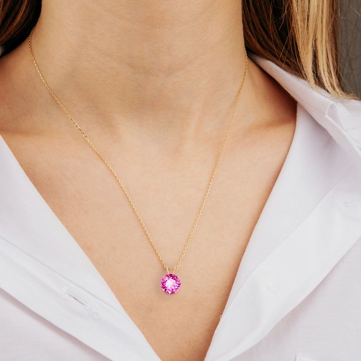 Woman wearing a 14K gold lab-created pink sapphire pendant necklace, bright candy pink, prong-set, cable chain.