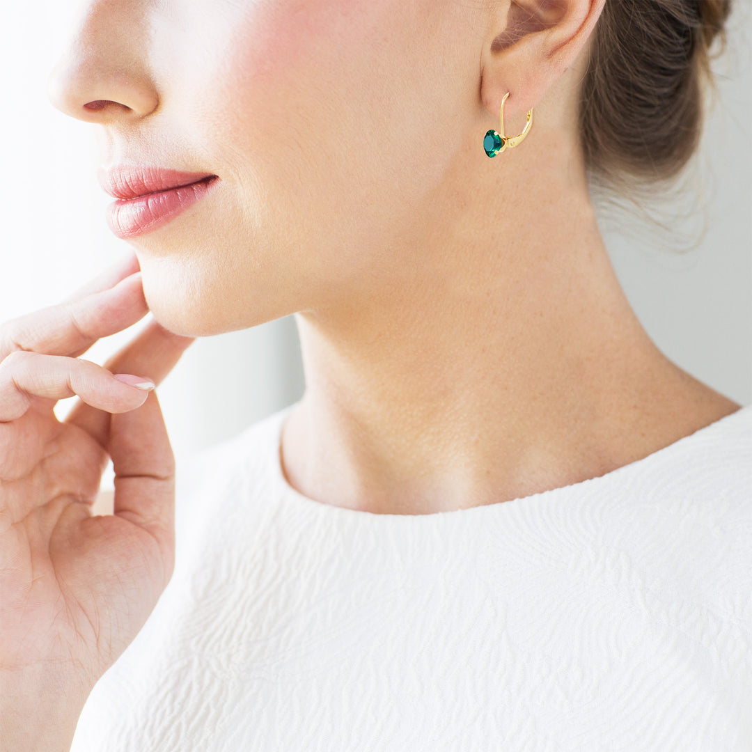 Model is wearing 14K yellow gold lab-grown emerald leverback earring, fingertip raised near chin as natural size reference