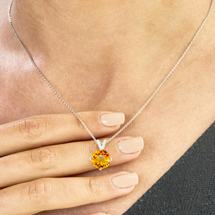 Hand holding an 8mm round citrine pendant necklace in sterling silver, with 4-prong setting and rolo chain.

